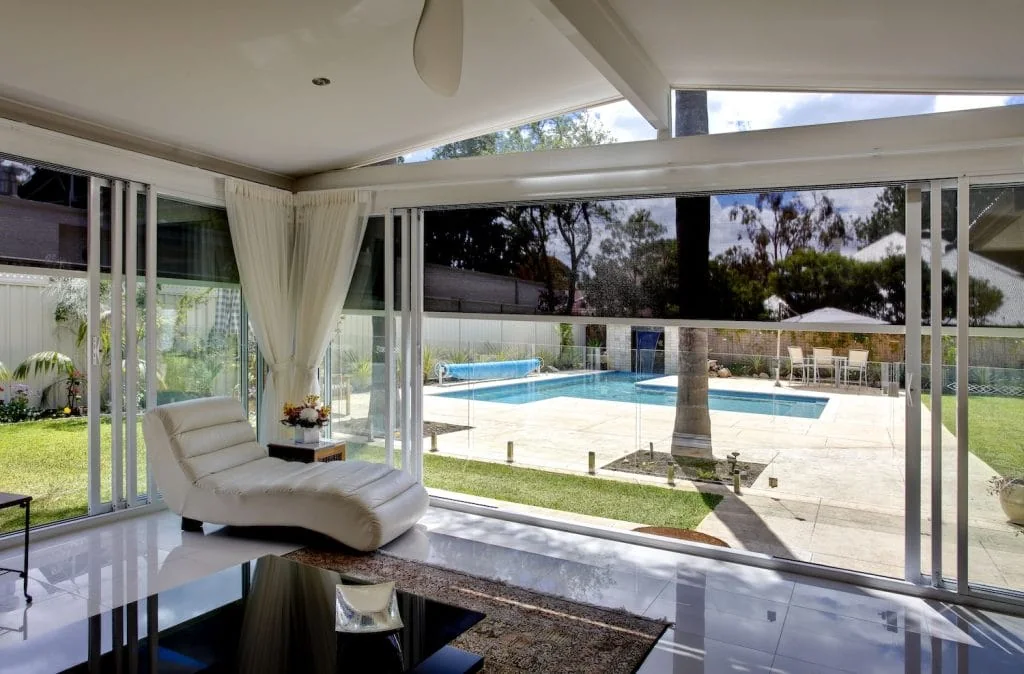 Motorized exterior zipper shades enclosing a covered patio beside a swimming pool.